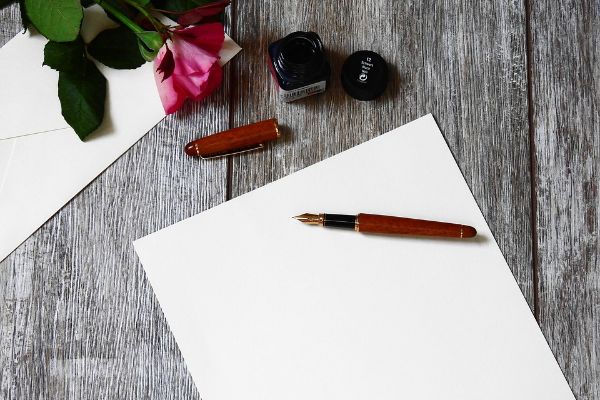 Fotografia di un quaderno bianco con una penna sopra e una rosa accanto