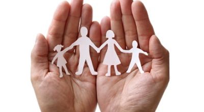 Mano che racchiude le sagome ritagliati di una famiglia