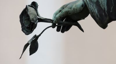 Fotografia della mano di una statua che tiene una rosa